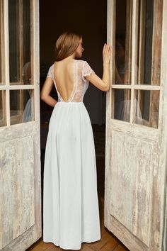 a woman in a white dress is looking out an open door with her back to the camera