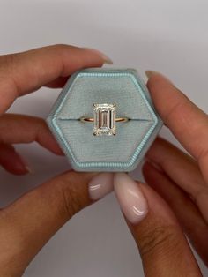 two hands holding an engagement ring with a green diamond in it's center,