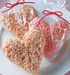 two heart shaped rice krispy treats on a white plate with red ribbon tied around them