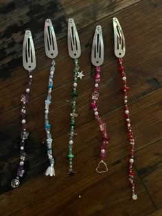 five different colored beads and silverware on a wooden table with one bead hanging from it's side