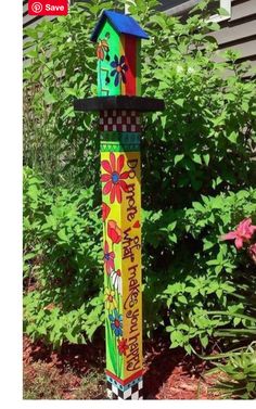 there is a colorful birdhouse on the pole in the yard with flowers and plants around it