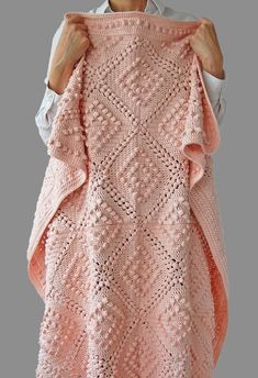 a woman holding up a pink crocheted shawl