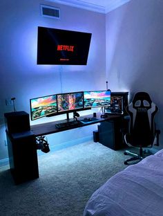 a bedroom with two computer monitors and a chair in front of the bed, all lit up by blue lights