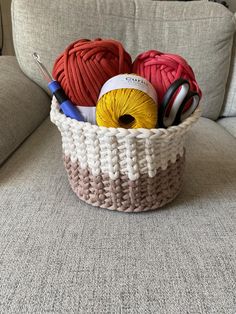 a basket filled with balls of yarn and crochet hooks on top of a couch