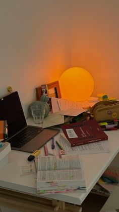 a laptop computer sitting on top of a white desk next to a lamp and books