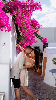 a man and woman kissing in front of pink bougaia flowers on the side of a building