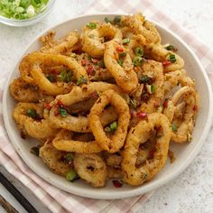 a white plate topped with fried onion rings next to a bowl of green onions and chopsticks