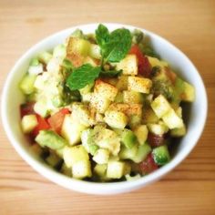 a white bowl filled with chopped vegetables and topped with green leafy garnish