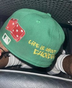 a person wearing a green hat with red dices and words on the front, while sitting in a car