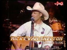 a man wearing a cowboy hat and holding a guitar in front of a tv screen