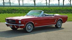 an old red mustang convertible parked in a parking lot