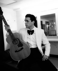 a man in a tuxedo is holding an acoustic guitar