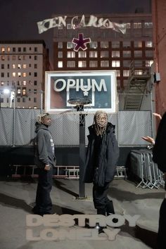 two men standing in front of a sign with the word open on it and one man holding a basketball hoop