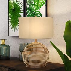 a table with a lamp on it next to a plant and pictures hanging on the wall