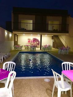 an empty swimming pool with white chairs and pink tablecloths on the tables next to it