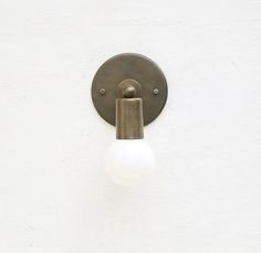 a light that is on the side of a white wall with a metal pole and glass ball