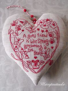 a heart shaped ornament with red thread on it and words written in the center