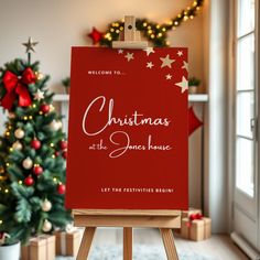 a red christmas sign sitting on top of a easel in front of a christmas tree