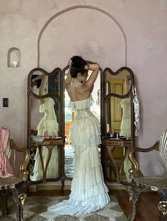 a woman standing in front of a mirror wearing a white dress with ruffles