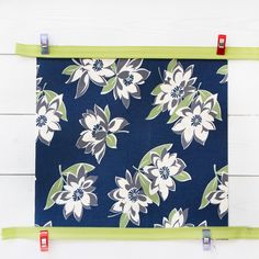 a blue and white flowered fabric hanging on a wall with two green clips in front of it