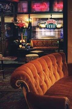 an orange couch sitting in front of a bar with neon signs on the wall behind it