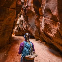 a woman with a blue backpack walking through a narrow canyon