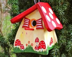 a birdhouse hanging from a tree with red roof and mushrooms painted on the side