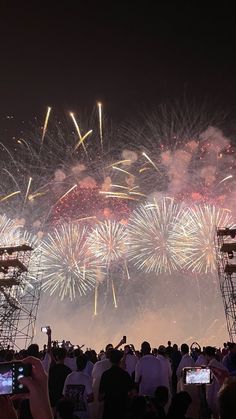 fireworks are lit up in the night sky and people are taking pictures with their cell phones