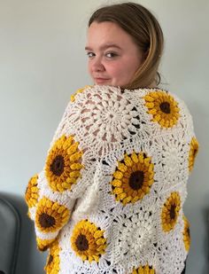 a woman wearing a white and yellow crocheted sweater with sunflowers on it