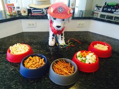 a dog statue sitting on top of a counter next to three bowls filled with food