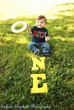 a young boy sitting in the grass with a frisbee and happy birthday sign