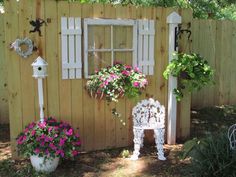 a white bench sitting in front of a wooden fence covered in flowers and potted plants