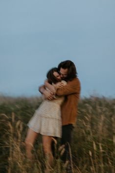 a man and woman hugging in tall grass with the sky in the backround