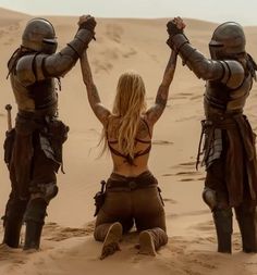 three women in armor are sitting on the sand with their hands up and arms raised