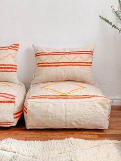 two pillows sitting next to each other on top of a wooden floor in front of a white wall