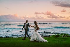 a bride and groom walking on the grass by the ocean at sunset with waves in the background