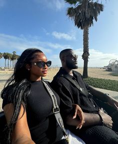 a man and woman sitting on the back of a convertible car in front of a palm tree