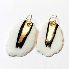 two white and black earrings with gold trims on top of each earring, sitting on a white surface