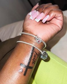 a woman's arm with tattoos on it and a cross tattooed on the wrist