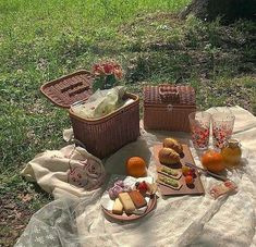 a picnic is set out on the grass with bread, fruit and juice in baskets