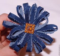 a hand holding a blue and white flower brooch with yellow center piece in it