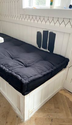 a black mattress sitting on top of a wooden floor next to a white wall and window