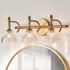 a bathroom light with three lights and a mirror on the wall above it in front of a window