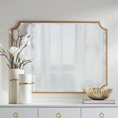 a white dresser topped with two vases filled with flowers next to a large mirror