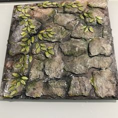 a stone wall with green plants growing on the top and bottom, in front of a black frame