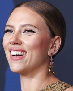 a close up of a person wearing earrings and smiling at the camera with her eyes closed