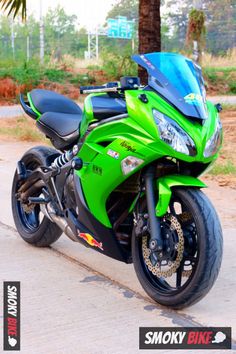 a green and black motorcycle parked on the side of the road next to a palm tree