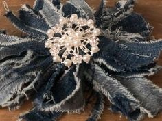 a close up of a flower on a wooden surface with fabric and pearls in the center