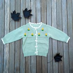 a green sweater sitting on top of a wooden floor next to two black maple leaves