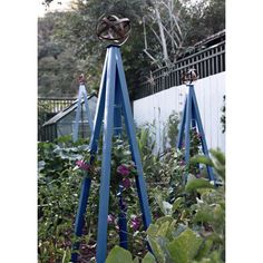 an outdoor garden with blue metal poles and plants in the foreground, next to a white fence